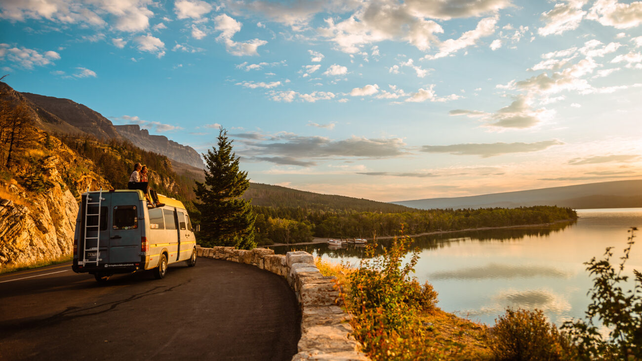 Paar sitzt auf Campervan vor Seepanorama